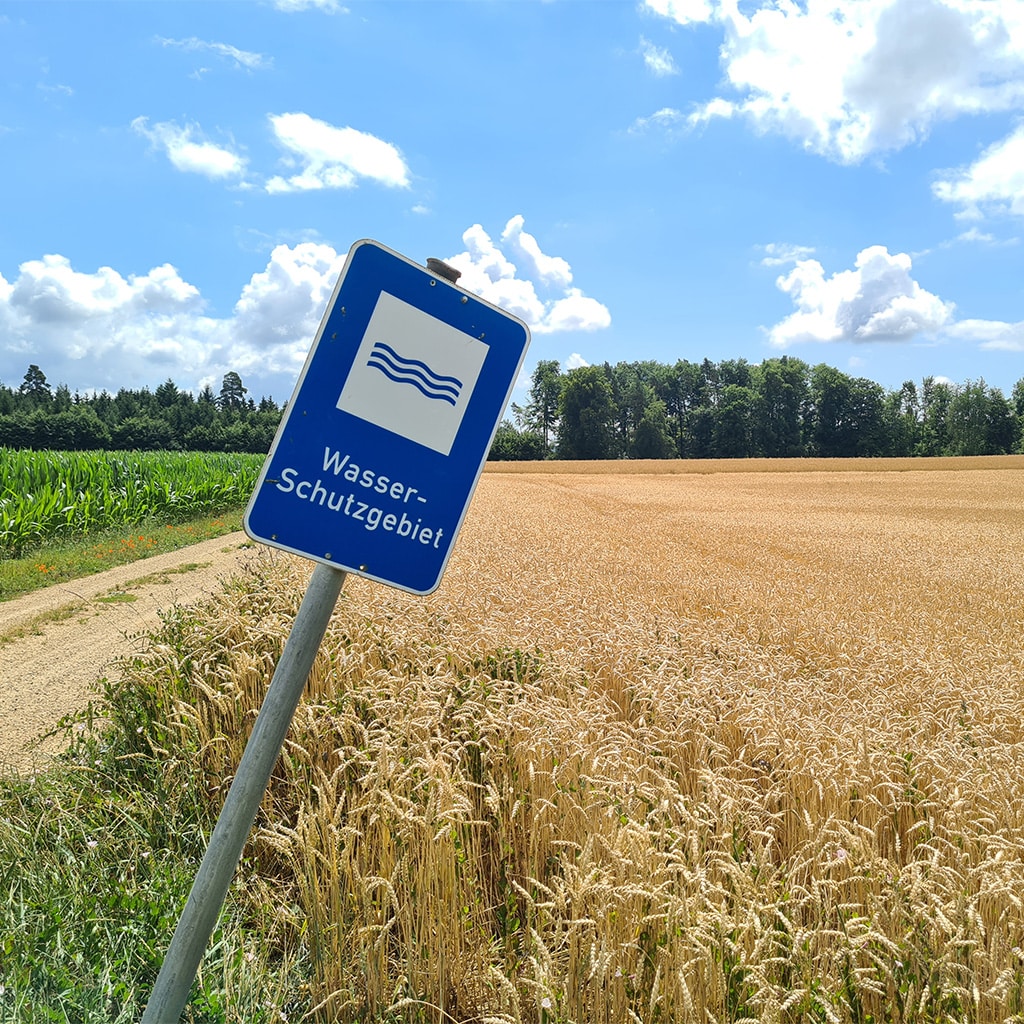 Hinweisschild ‚Wasserschutzgebiet‘ neben Getreidefeld mit Wald im Hintergrund